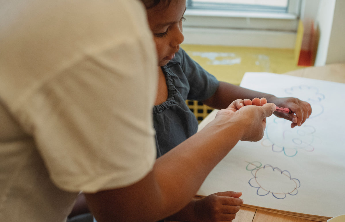 Crop anonymous female in white tshirt helping daughter drawing with color pencils on paper